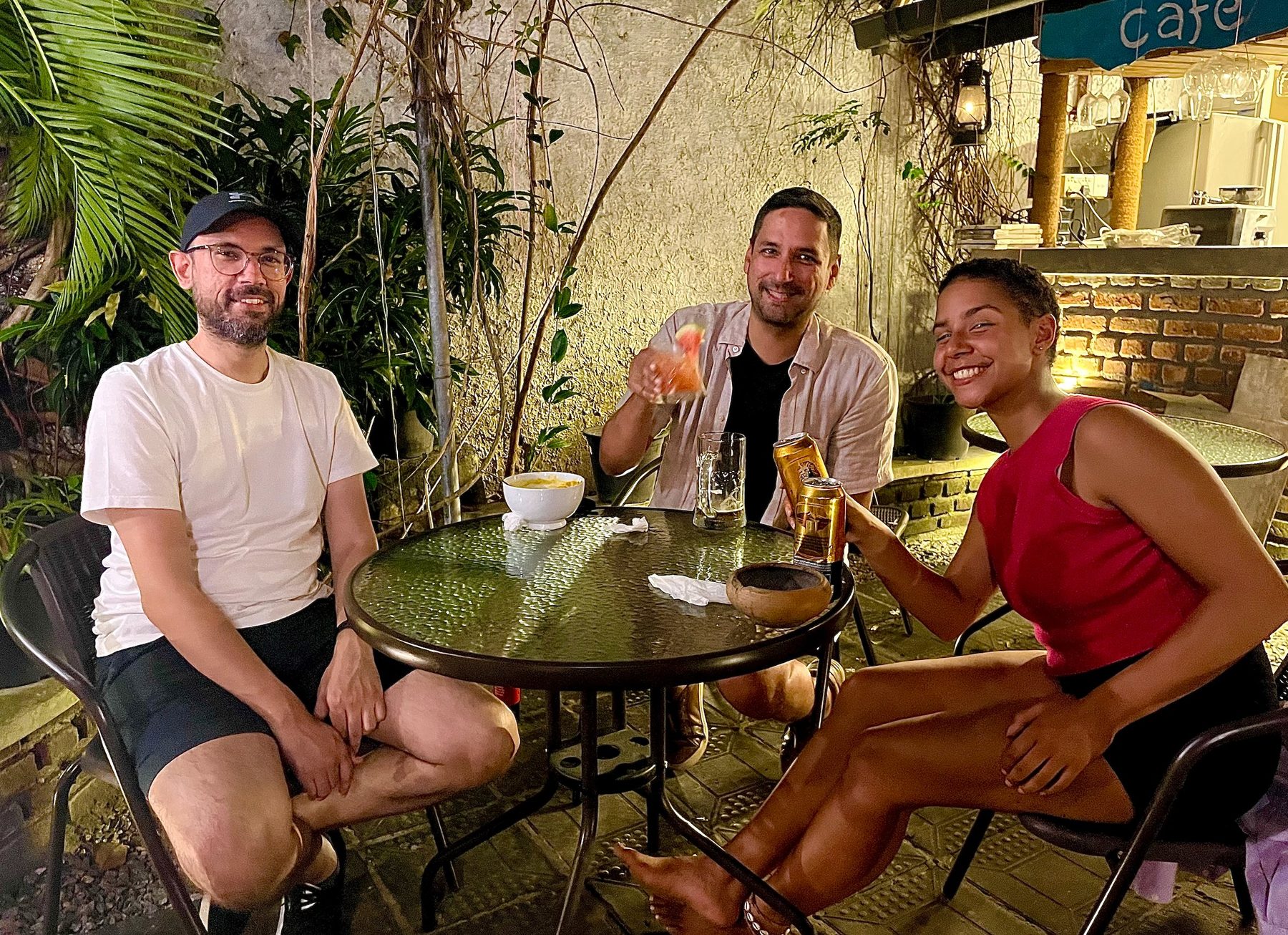 Three guests at a garden table at Seconds Colombo, café signage behind them, evening light