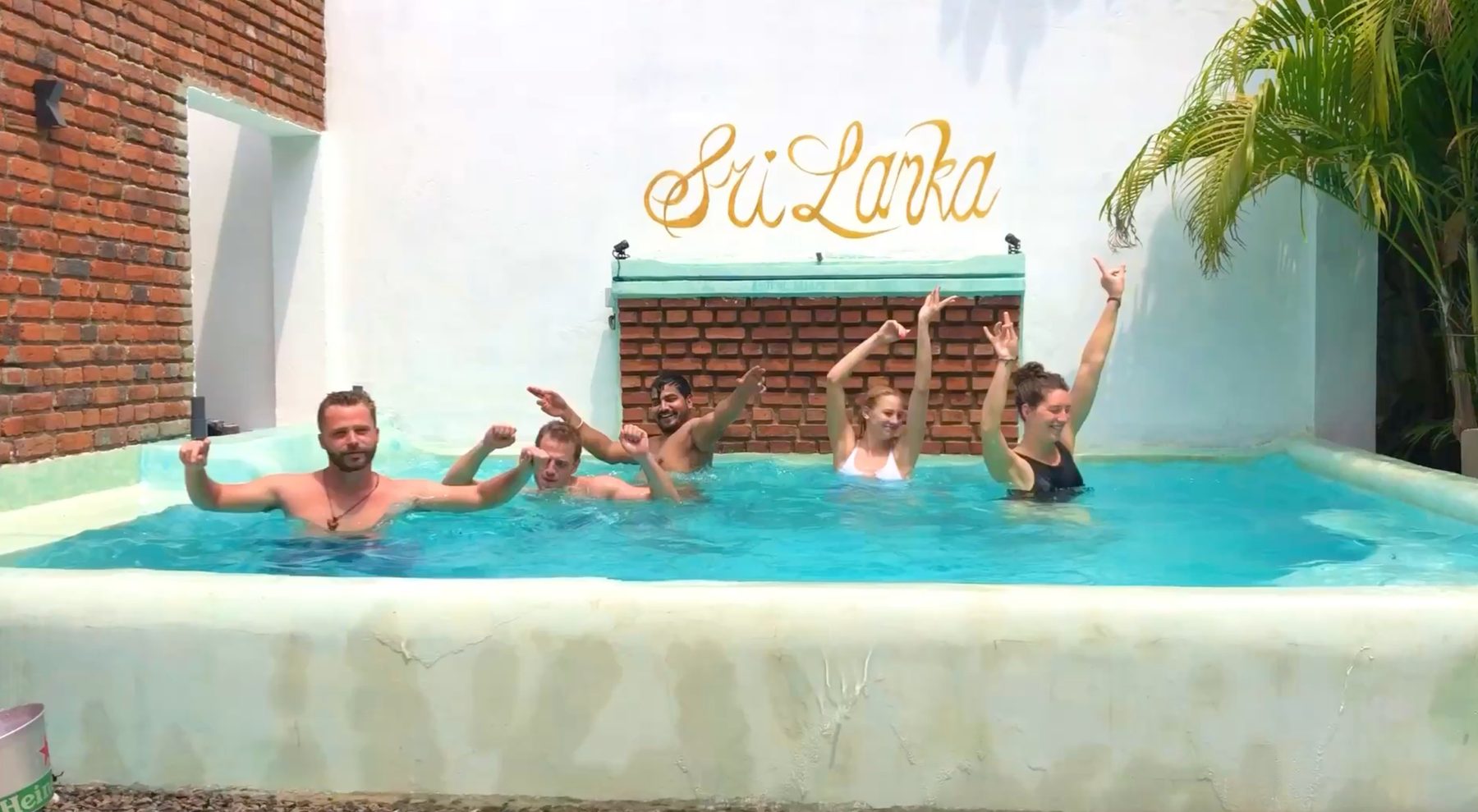 Five guests laughing in the plunge pool at Seconds Colombo Boutique Hotel — coconut palms above, gold sign on the wall