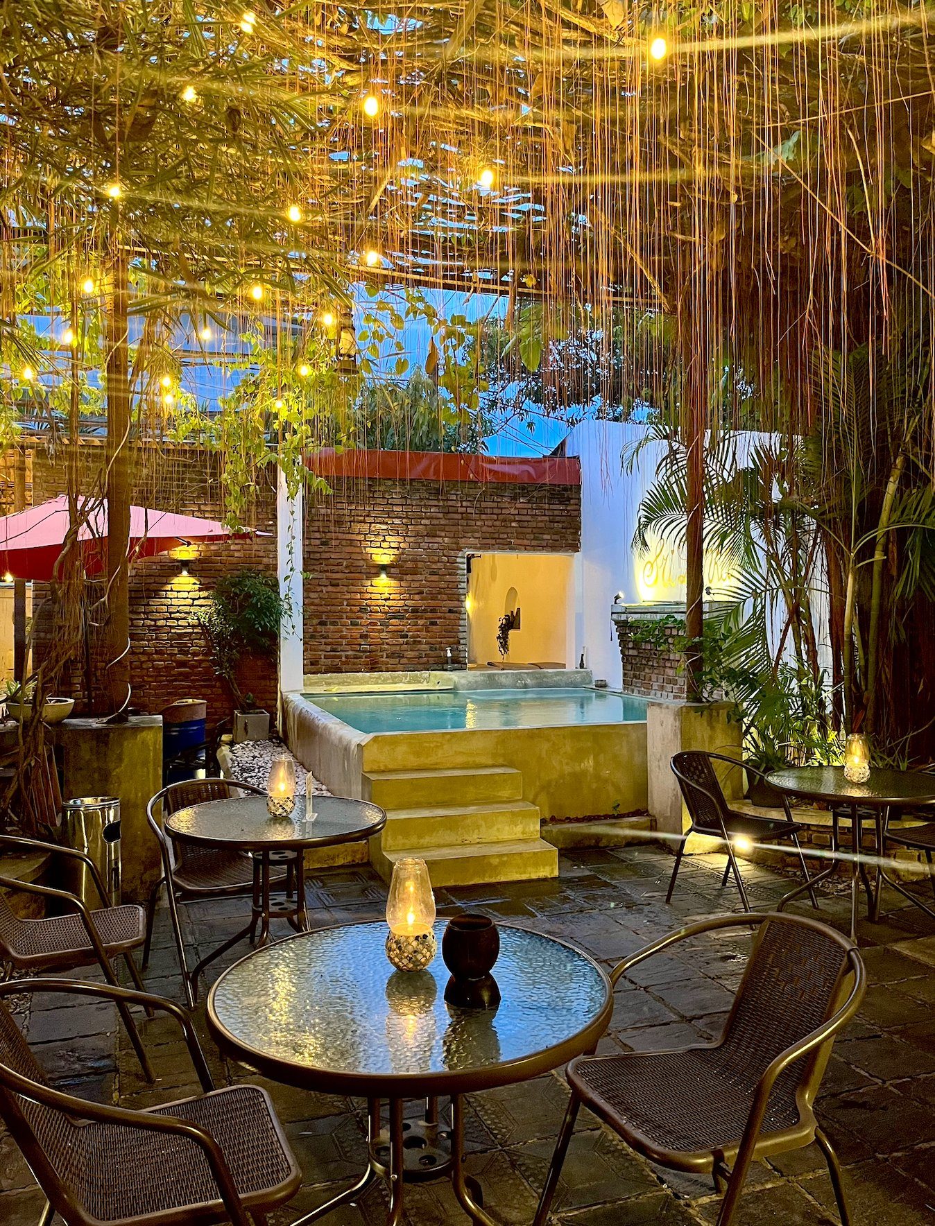 The garden at Seconds Colombo — fairy lights between trees, full restaurant tables, brick walls, evening light
