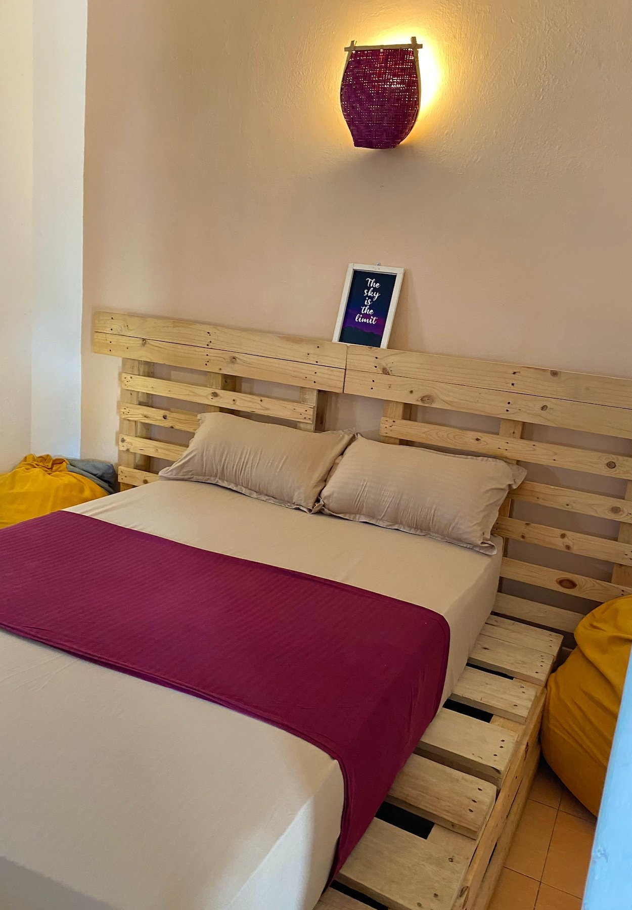Serenity Double Room at Seconds Colombo — pallet-bed with magenta runner, woven wall lamp, yellow beanbags, 'the sky is the limit' artwork